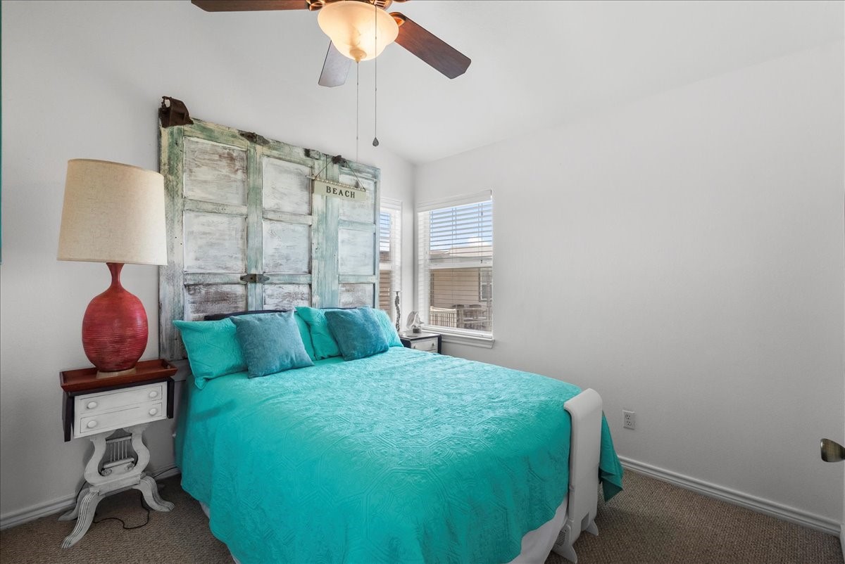 819 Seashell Drive Surfside Beach, TX 77541 - Photo 9 of 27 Cozy bedroom with a beachy vibe, featuring a turquoise bedspread and rustic shutter headboard. Bright windows and a ceiling fan enhance the airy feel.