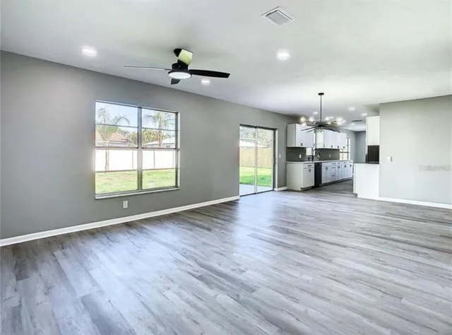 an empty room with wooden floor a ceiling fan and windows