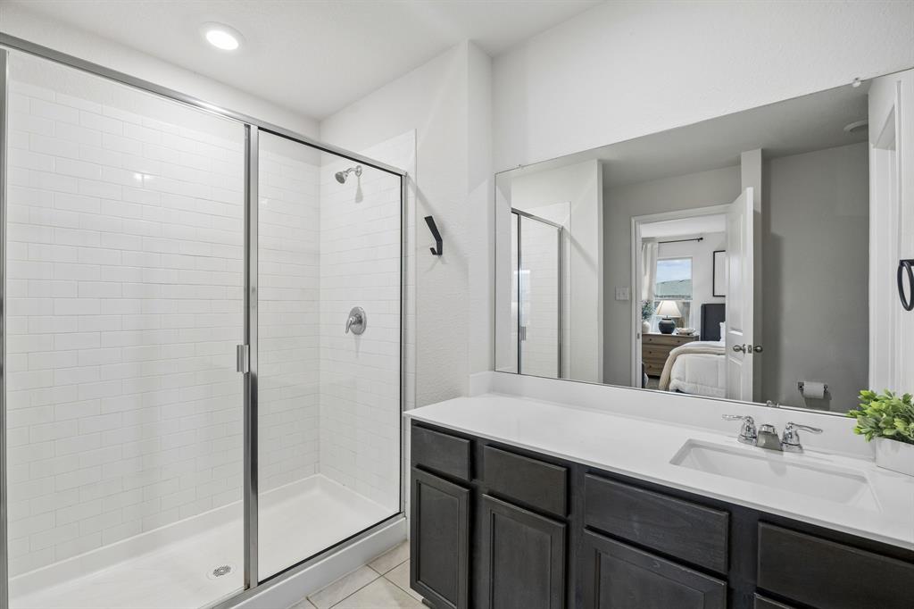 1107 Ringgold Road Forney, TX 75126 - Photo 7 of 27 Bathroom featuring a glass-enclosed shower with subway tile surround, a single vanity with a white countertop, dark wood-finish cabinetry, and a large wall-mounted mirror