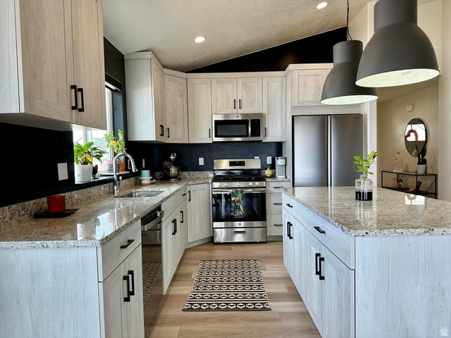 4349 Half Mile Road East Enoch, UT 84721 - Photo 8 of 36 Kitchen with light stone counters, stainless steel appliances, vaulted ceiling, a center island, and light wood-style floors