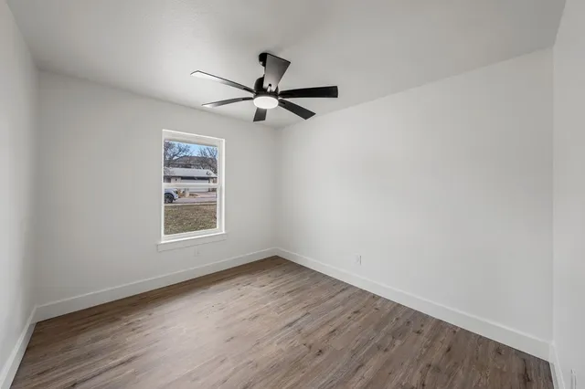 an empty room with wooden floor fan and windows