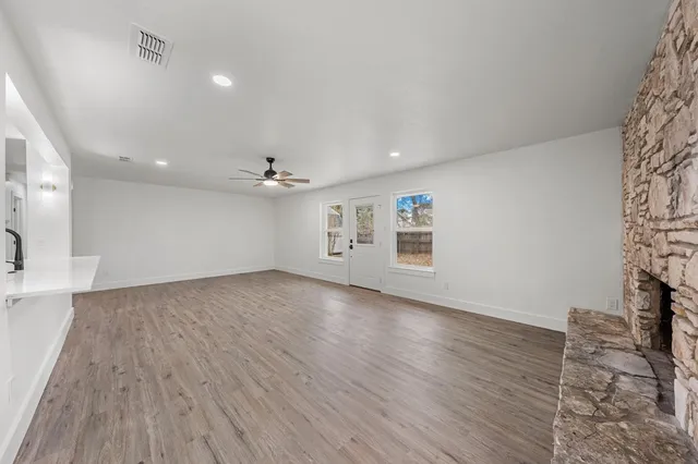 an empty room with wooden floor ceiling fan and windows