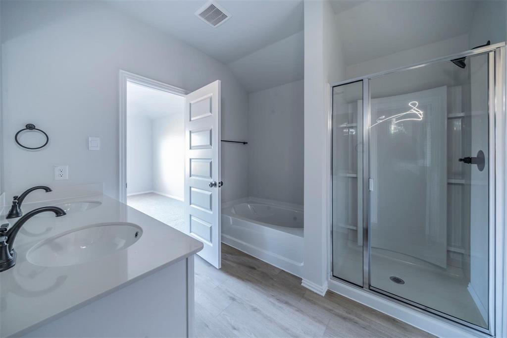 516 Ridgewood Drive Van Alstyne, TX 75495 - Photo 13 of 25 Modern bathroom featuring a dual vanity with white countertops and matte black fixtures, a built-in tub, a glass-enclosed shower, and light wood-finish flooring