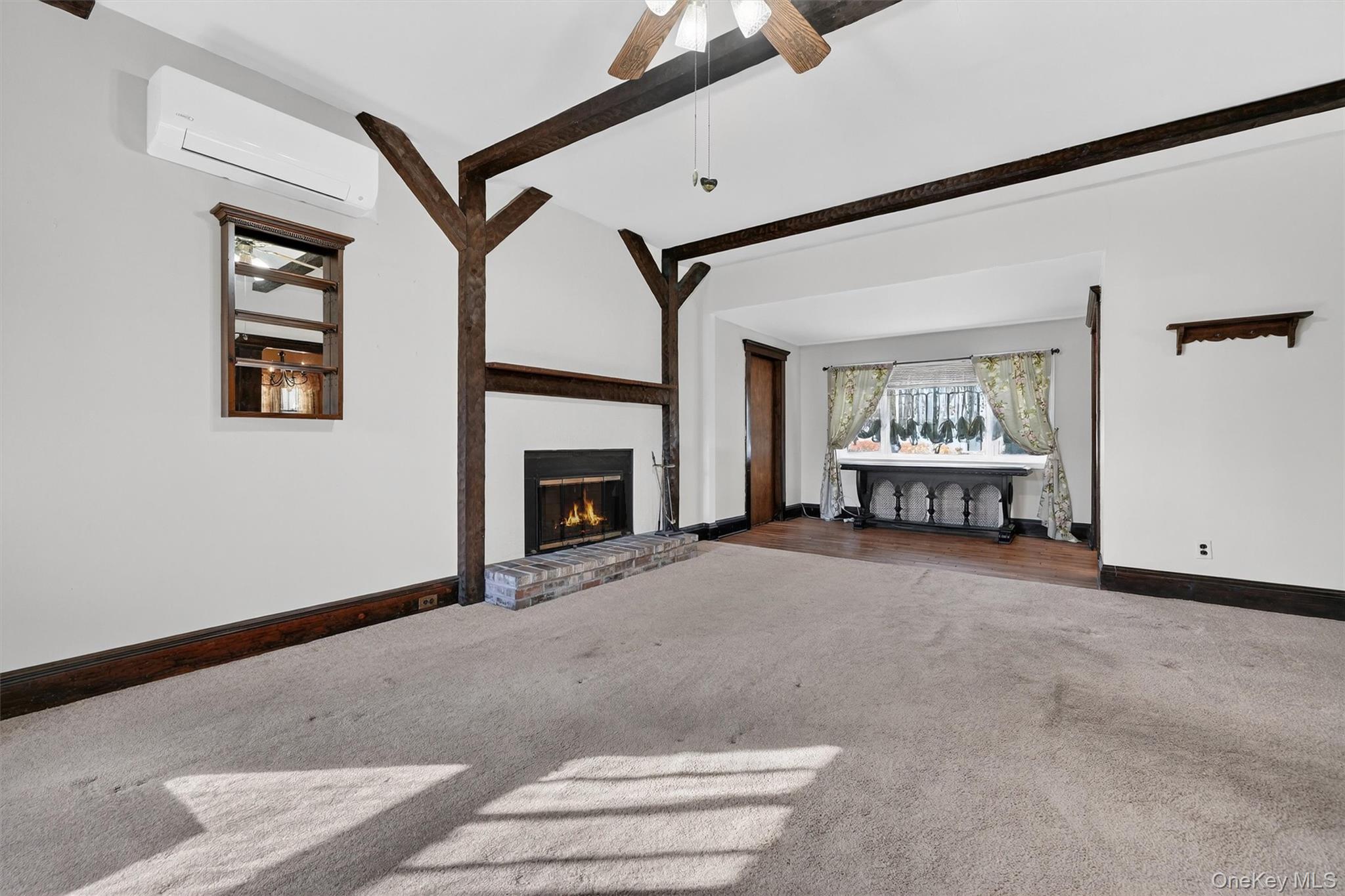 165 Wayne Avenue Suffern, NY 10901 - Photo 13 of 38 Unfurnished living room with a brick fireplace, beam ceiling, carpet floors, a wall mounted air conditioner, and ceiling fan