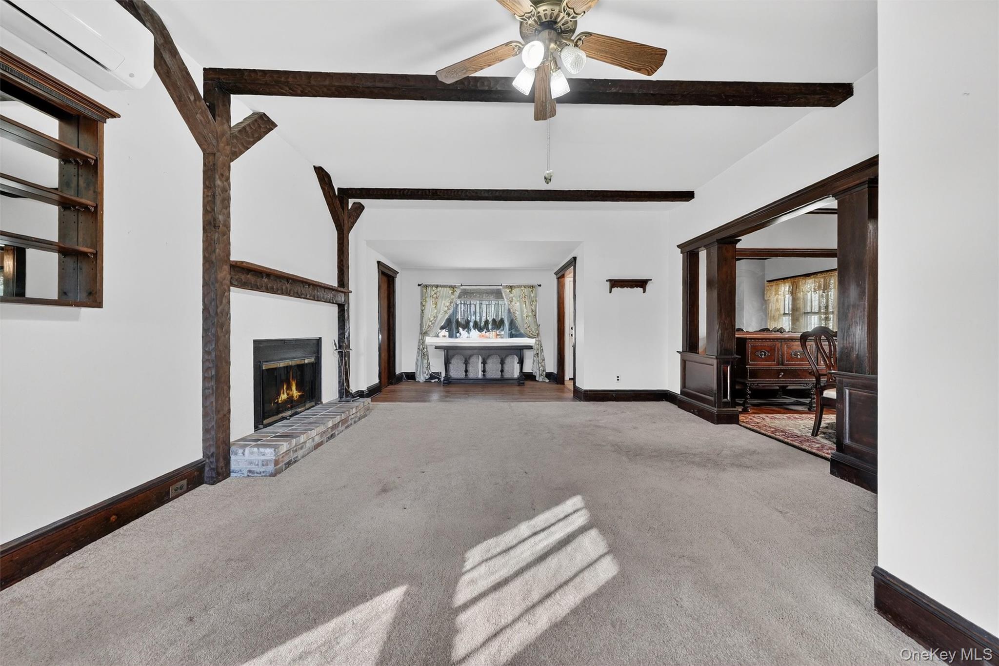 165 Wayne Avenue Suffern, NY 10901 - Photo 15 of 38 Unfurnished living room featuring beam ceiling, a wall mounted AC, carpet floors, a brick fireplace, and ceiling fan