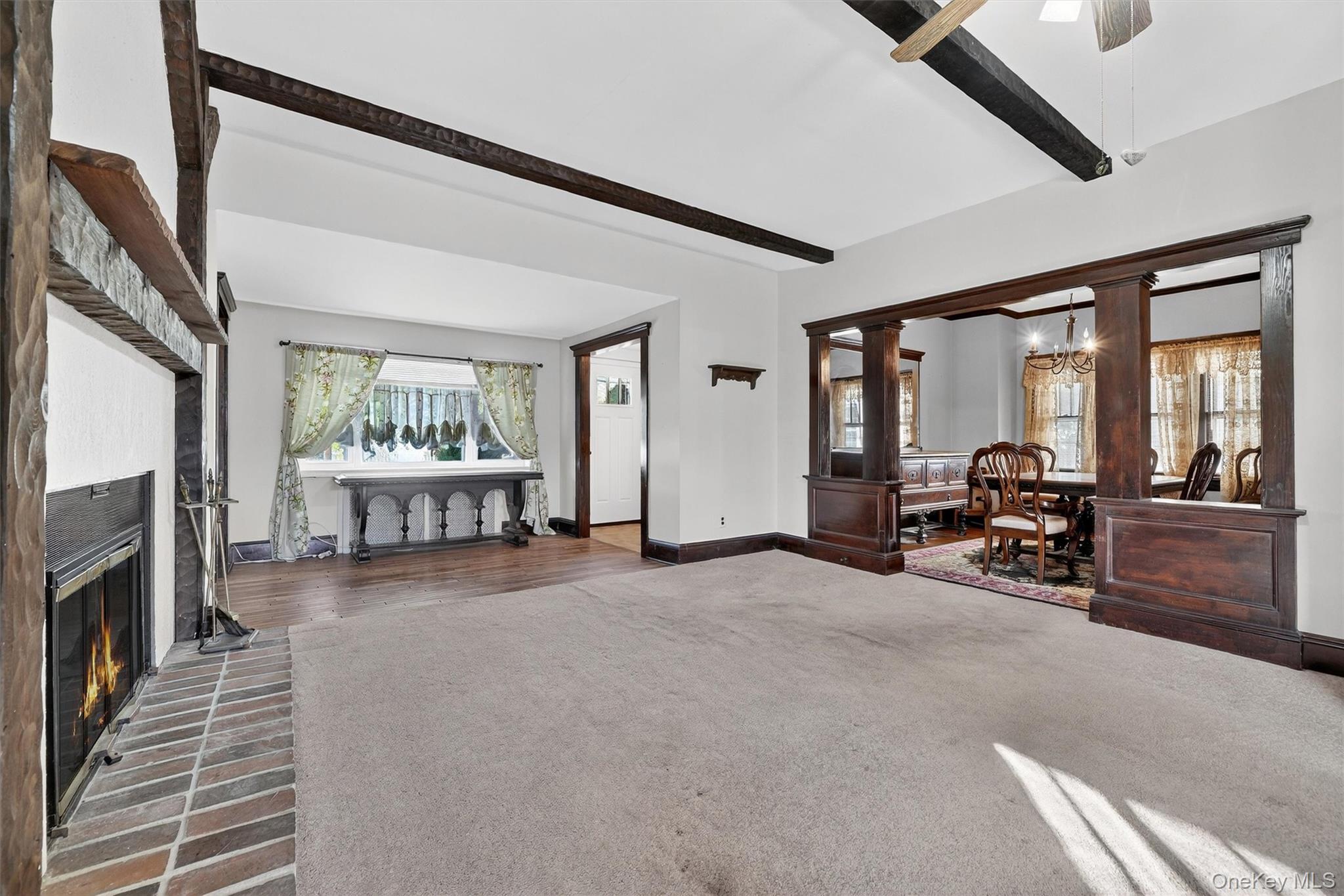 165 Wayne Avenue Suffern, NY 10901 - Photo 16 of 38 Carpeted living room featuring beamed ceiling, a brick fireplace, decorative columns, and a chandelier