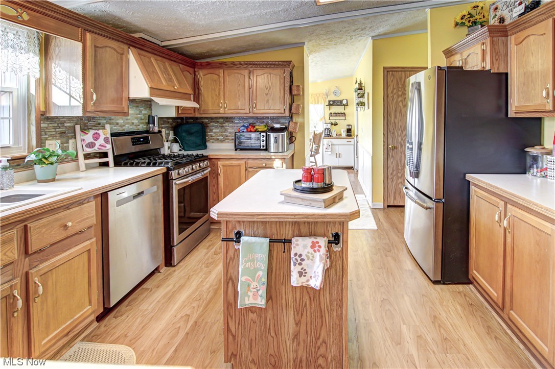 9459 Stone Road Litchfield, OH 44253 - Photo 4 of 50 Kitchen with light hardwood / wood-style flooring, a kitchen island, a textured ceiling, vaulted ceiling, and appliances with stainless steel finishes