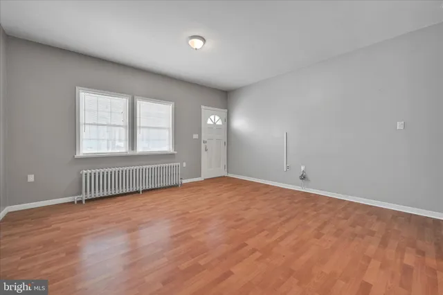 a view of empty room with wooden floor and kitchen