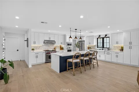 a large white dining hall with stainless steel appliances granite countertop a stove oven a sink dishwasher with a dining table and chairs