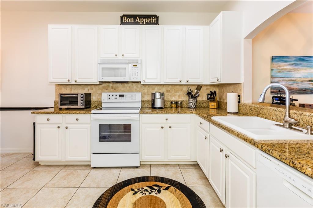 14151 Fall Creek Court Naples, FL 34114 - Photo 6 of 35 a kitchen with granite countertop white cabinets and white appliances