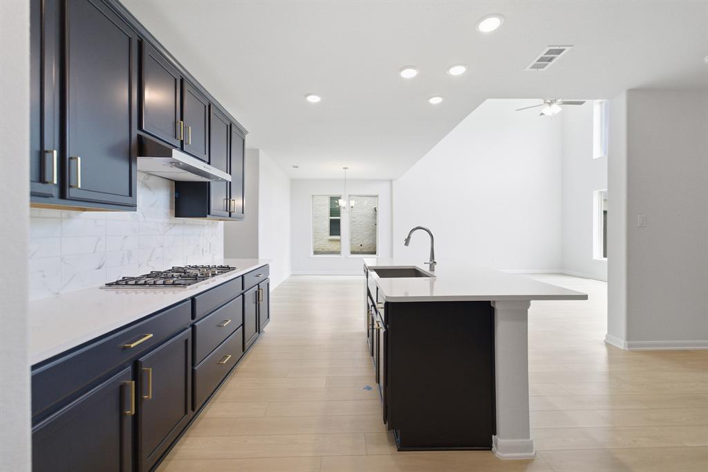 1908 Sangallo Lane Celina, TX 75009 - Photo 20 of 35 Modern kitchen featuring dark cabinetry with gold-tone hardware, white countertops, and a subway tile backsplash