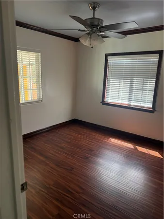 an empty room with wooden floor chandelier fan and windows
