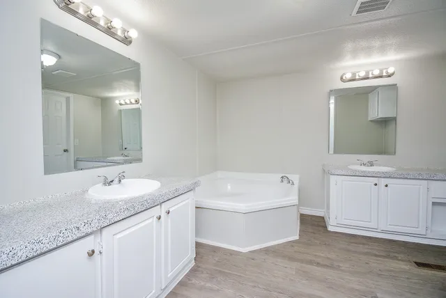a bathroom with a granite countertop double vanity sink mirror and bathtub