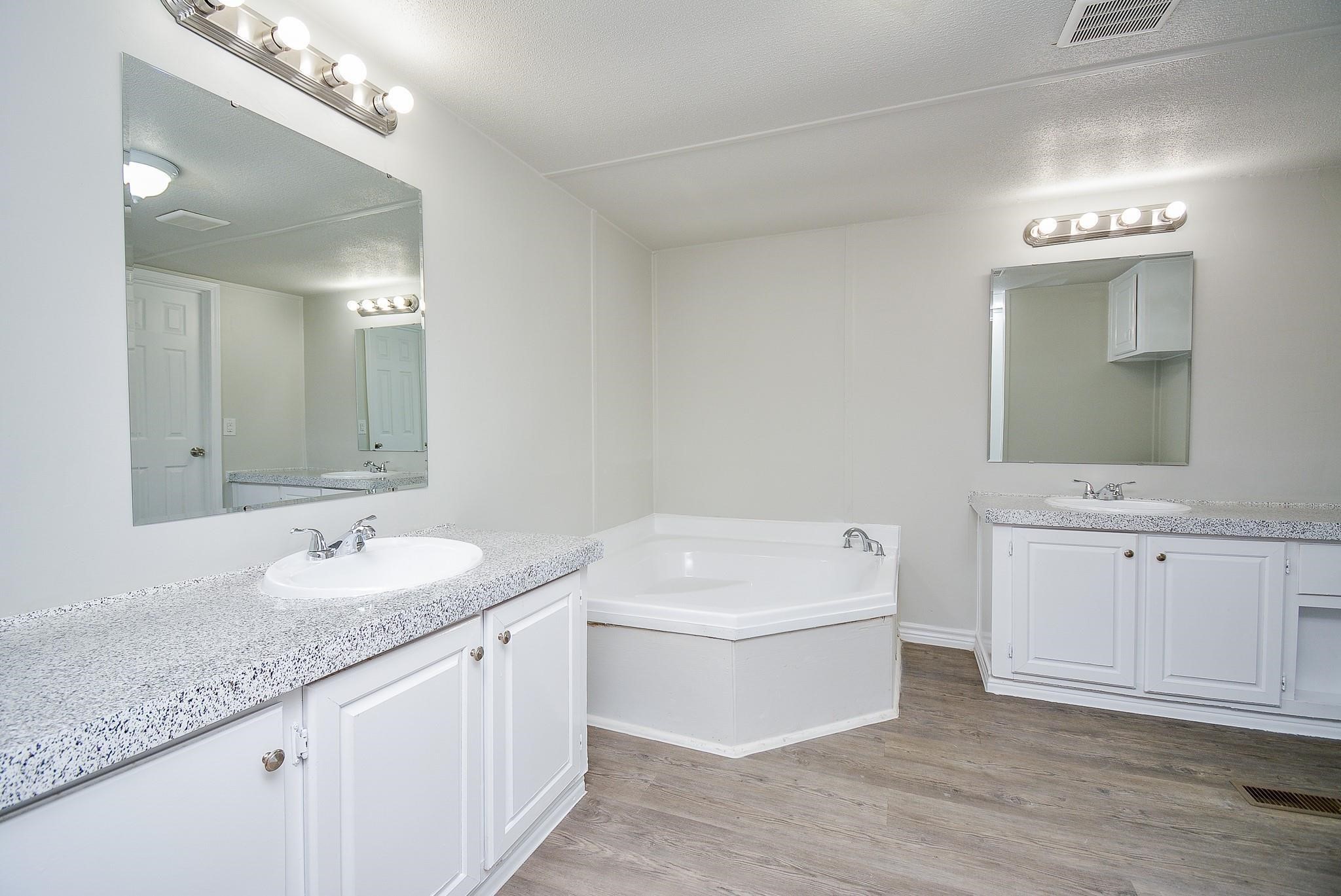 a bathroom with a granite countertop double vanity sink mirror and bathtub