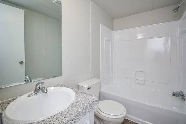 a bathroom with a granite countertop sink a toilet a mirror and bathtub