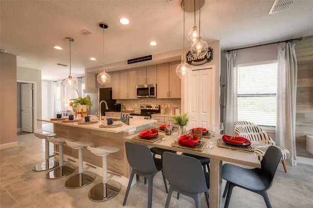 a kitchen with stainless steel appliances a dining table chairs stove refrigerator and cabinets