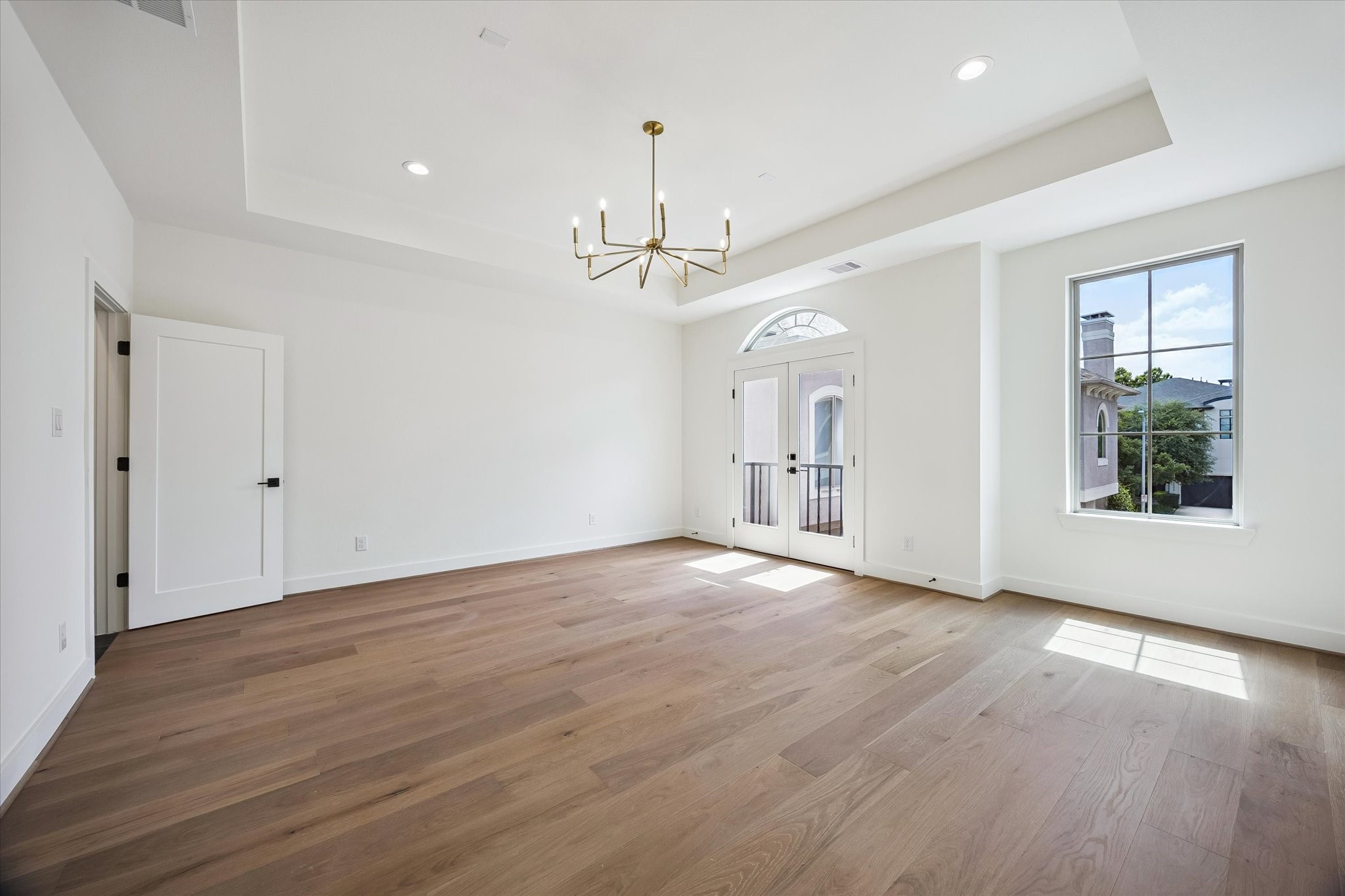 5329 Dora Street Houston, TX 77005 - Photo 22 of 43 Step into the serene primary suite, where an elegant tray ceiling and abundant natural light highlight the rich floors. French doors open to a charming Juliet balcony overlooking the peaceful, gated community, quietly nestled within one of the Museum District's most desirable neighborhoods.