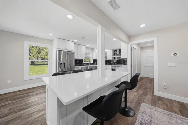 a kitchen with stainless steel appliances a stove top oven a sink dishwasher a dining table and chairs with wooden floor