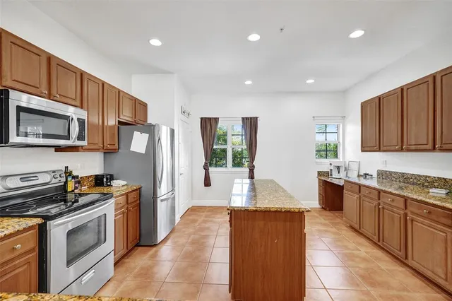 a large kitchen with stainless steel appliances granite countertop a stove top oven a refrigerator a sink and dishwasher wooden cabinets with wooden floor