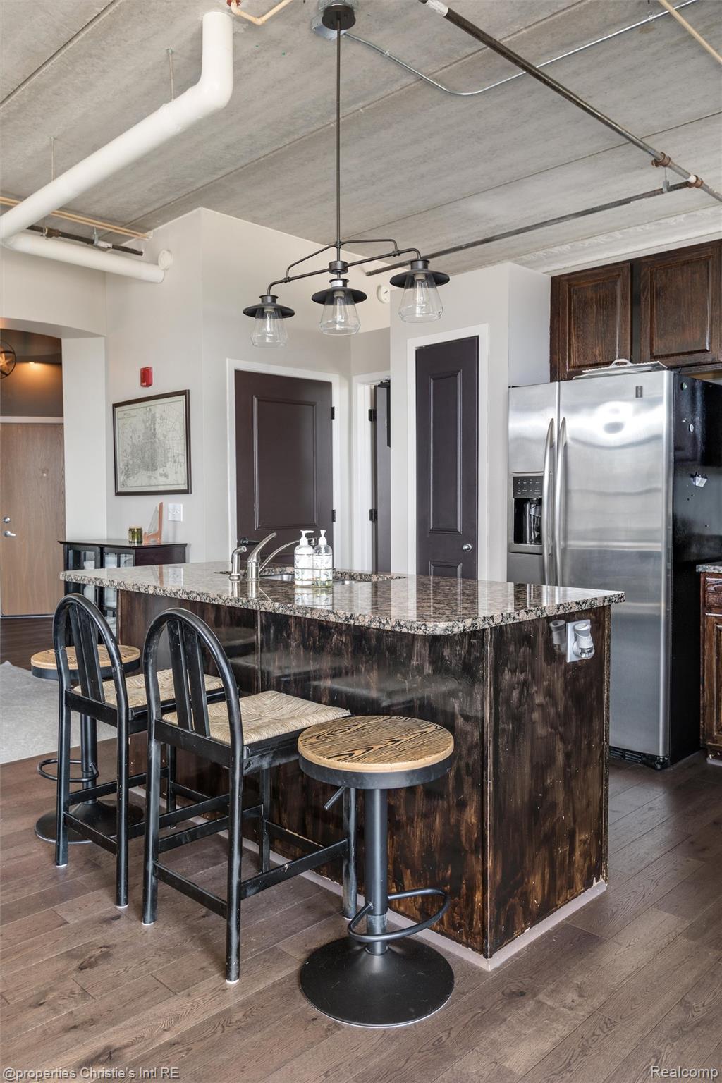 66 Winder Street, Unit 332 Detroit, MI 48201 - Photo 10 of 30 Kitchen with dark wood finish cabinets, stainless steel fridge with ice dispenser, dark wood-type flooring, and a breakfast bar area
