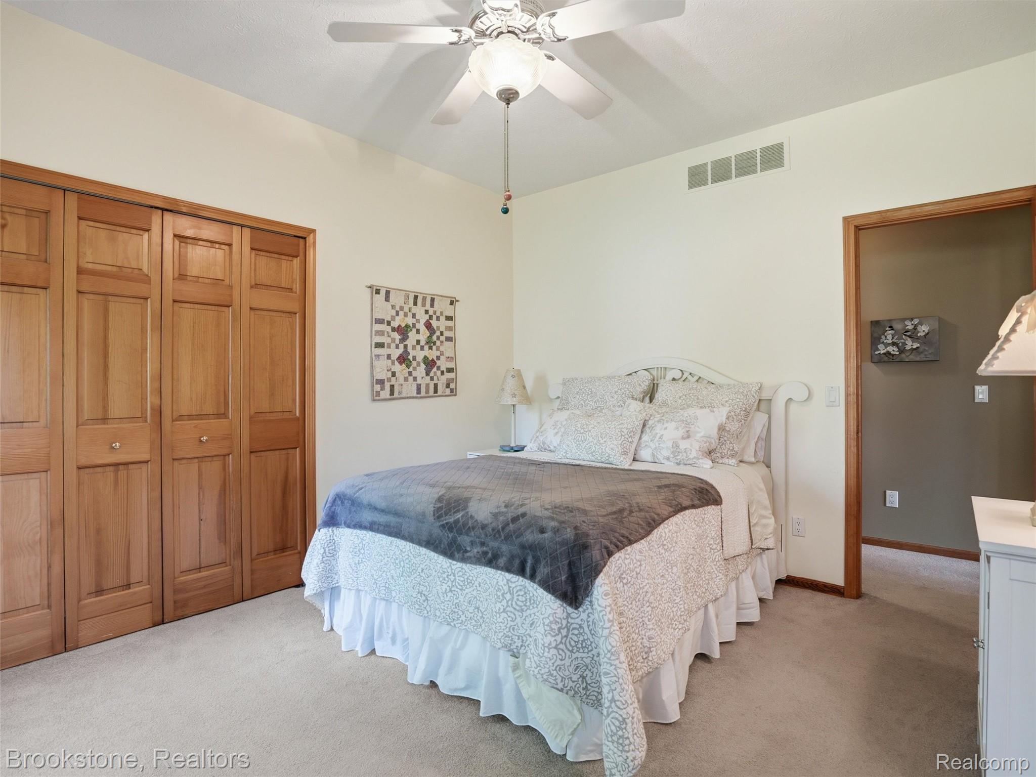 9523 Quail Ridge Run Brighton, MI 48114 - Photo 30 of 50 Carpeted room featuring a white ceiling fan with integrated lighting, natural wood bi-fold closet doors, and light-toned wall paint
