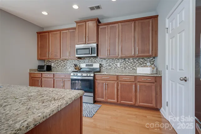 a kitchen with stainless steel appliances granite countertop a stove a sink dishwasher and a microwave oven with white cabinets