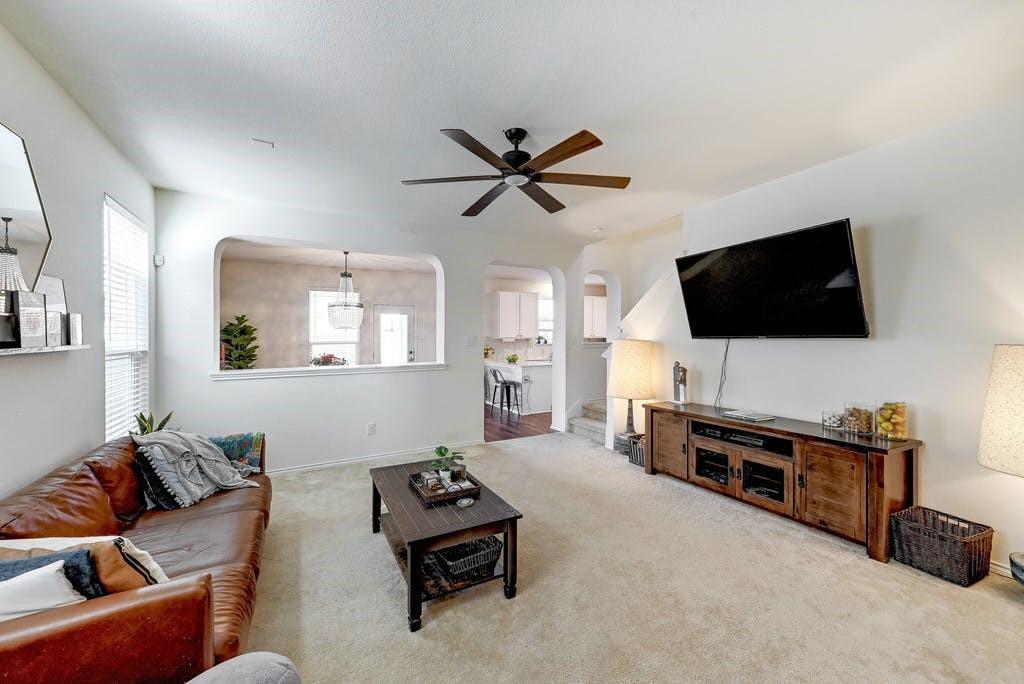 13916 Inaugural Street Manor, TX 78653 - Photo 5 of 28 A comfortable living space featuring soft carpeting and a ceiling fan, seamlessly connecting to an adjoining kitchen through an arched entryway.