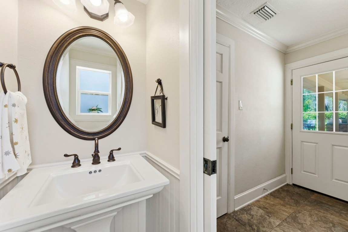 20 Falling Star Road The Woodlands, TX 77381 - Photo 19 of 44 Adjacent to the laundry room is a elegant half-bath featuring a pedestal sink, an oval mirror, and tasteful lighting. The space is clean and inviting, with neutral tones and stylish fixtures.