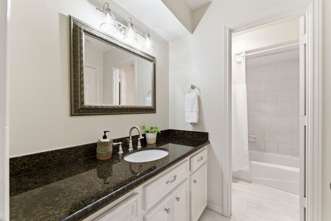 20 Falling Star Road The Woodlands, TX 77381 - Photo 29 of 44 This secondary bathroom features a sleek black granite countertop with a white vanity, a large framed mirror, and modern lighting. It includes a tub/shower and white tiled walls, offering a clean and elegant look.