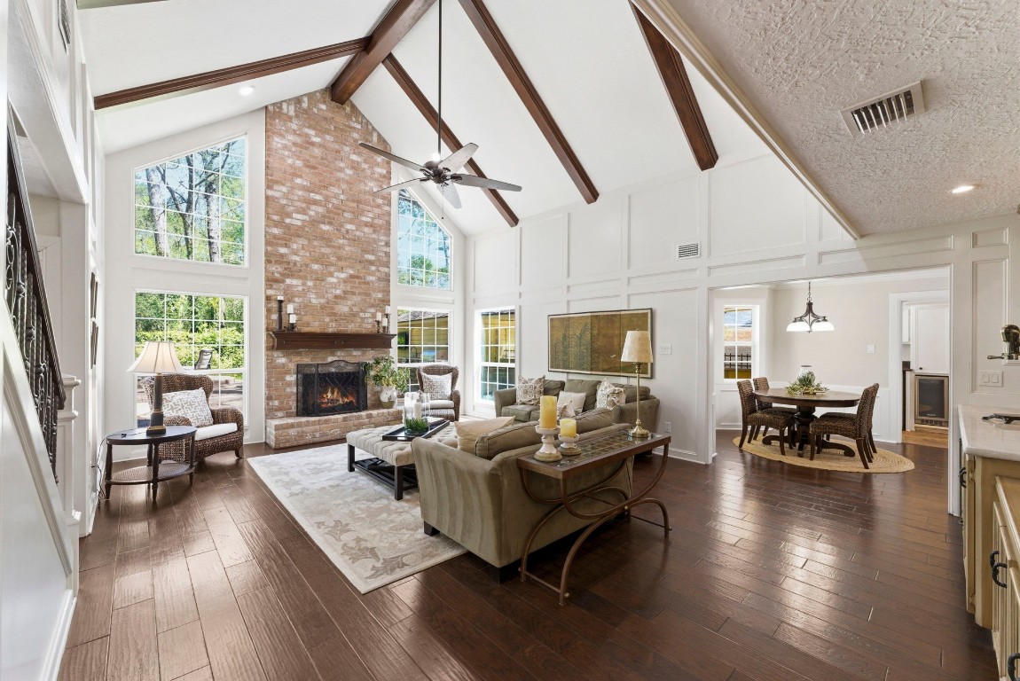 20 Falling Star Road The Woodlands, TX 77381 - Photo 8 of 44 This inviting living space features a high vaulted ceiling with exposed wooden beams and a striking brick fireplace. Large windows provide ample natural light, while the open layout connects seamlessly to a cozy dining area. Rich hardwood floors and elegant decor create a warm, sophisticated atmosphere.