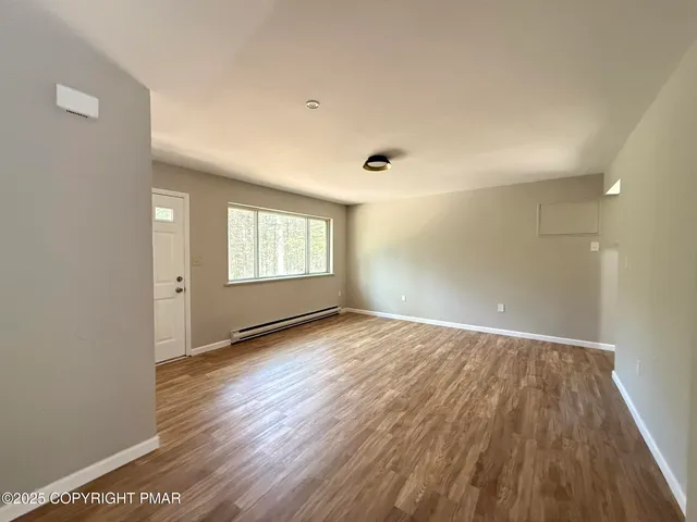 a view of an empty room with wooden floor and a window
