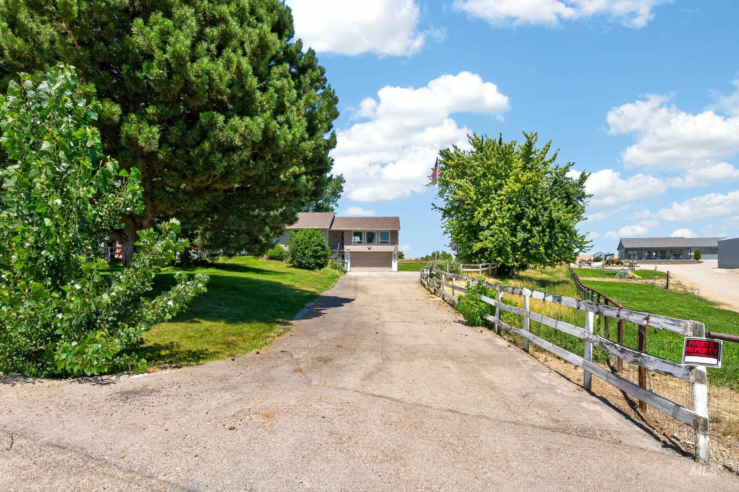 9696 Gloria Road Middleton, ID 83644 - Photo 3 of 50 Paved driveway with a wooden fence, bordered by mature trees and a manicured lawn