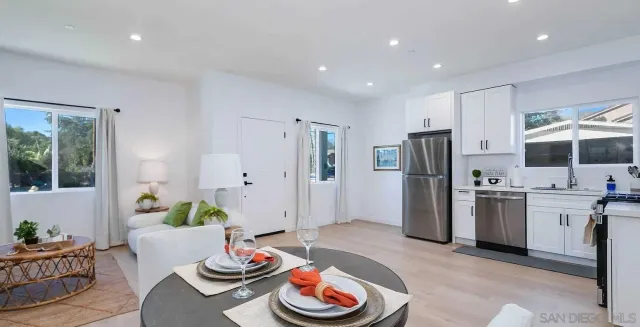 a living room with stainless steel appliances furniture a rug and a kitchen view