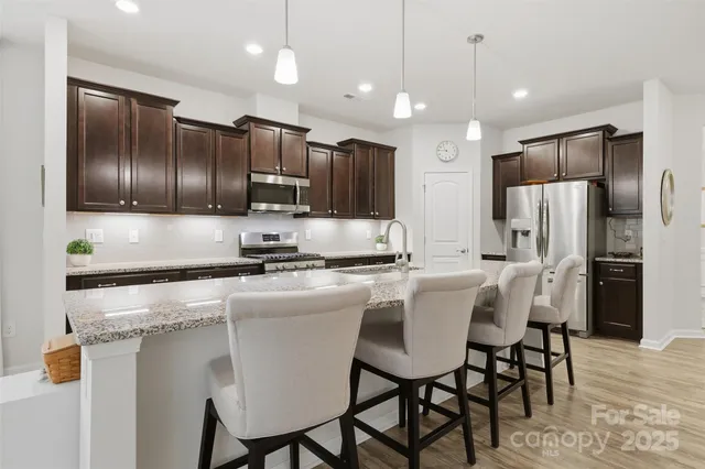 a kitchen with stainless steel appliances granite countertop a sink a stove a refrigerator with island and chairs