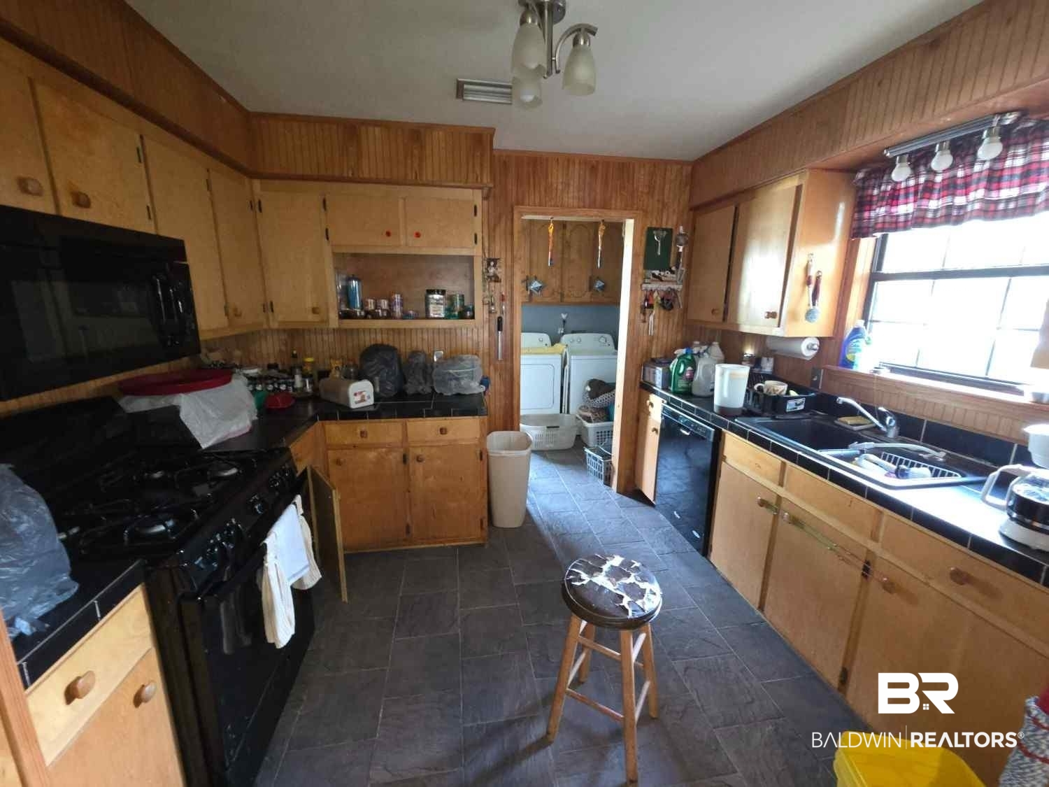 5120 West Celtic Drive Mobile, AL 36619 - Photo 7 of 27 Kitchen featuring washer and dryer, tile counters, black appliances, and wood walls