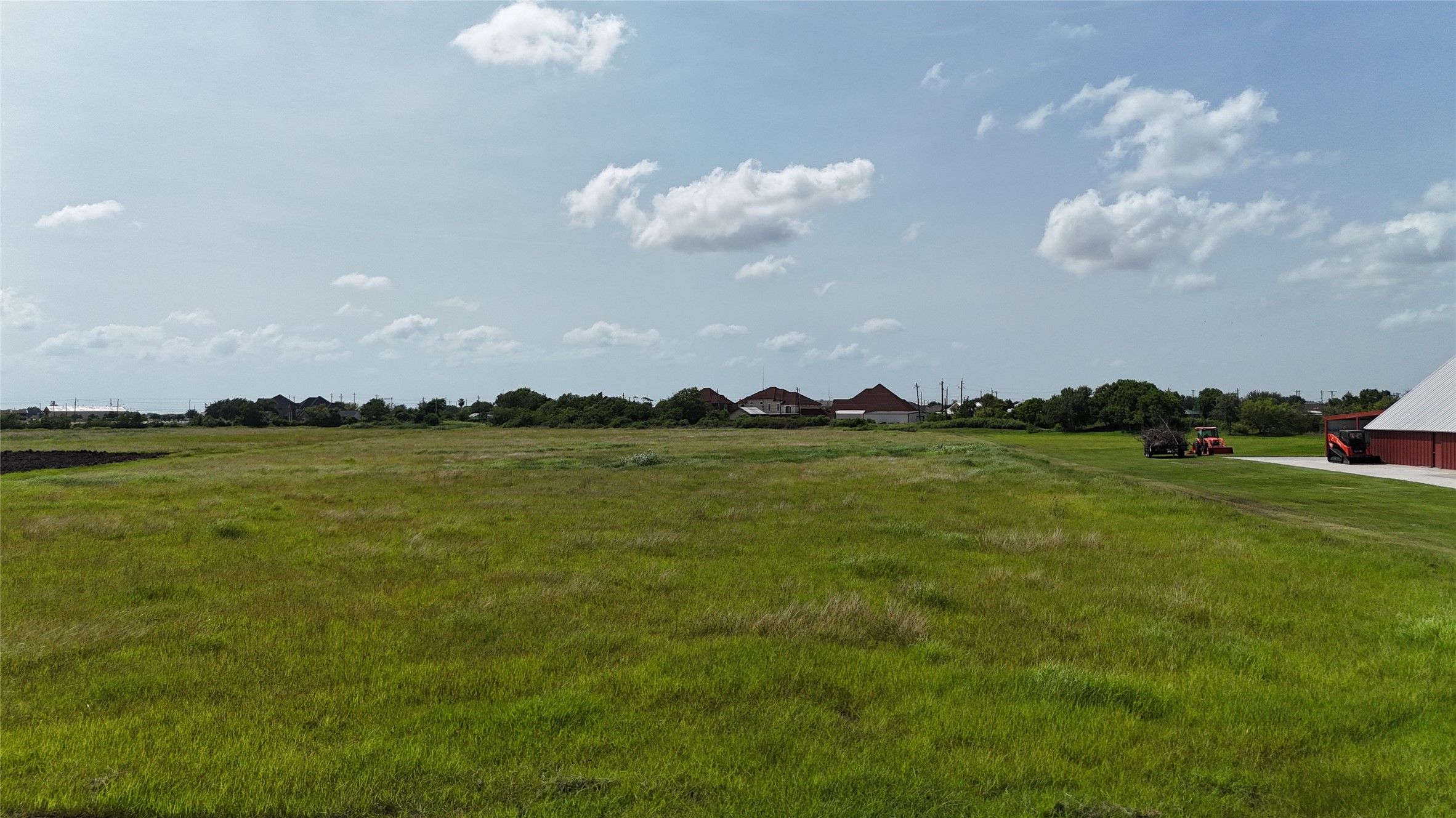 305 Bayshore Road Palacios, TX 77465 - Photo 3 of 25 A verdant, open field extends towards distant residential structures beneath a wide, open sky.