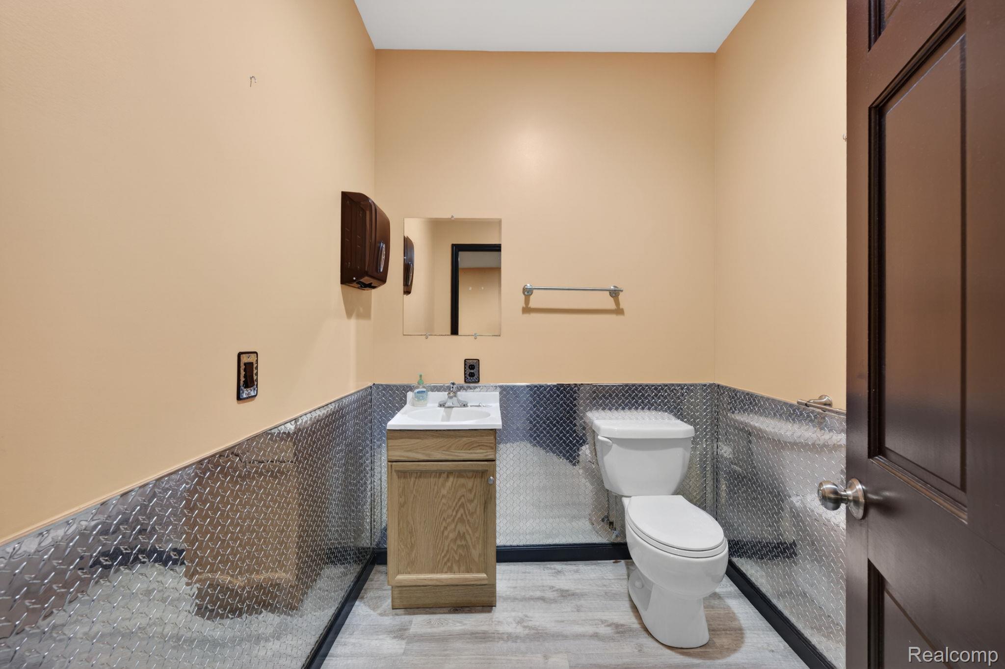 9353 Hill Road Swartz Creek, MI 48473 - Photo 84 of 98 Restroom featuring diamond plate wainscoting, light wood-finish flooring, a wood-finish vanity with a white countertop and integrated sink, a wall-mounted mirror, and a dark paneled door