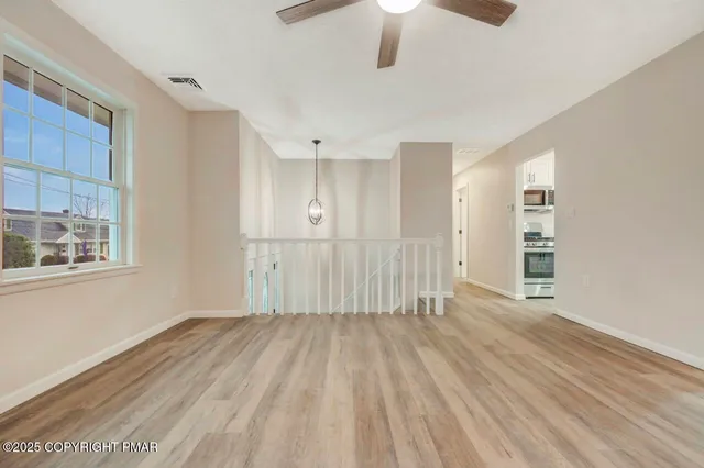 a view of an empty room with wooden floor and a ceiling fan
