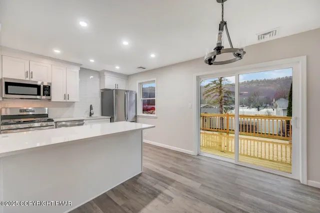 a kitchen with stainless steel appliances granite countertop a refrigerator a stove and white cabinets with wooden floor