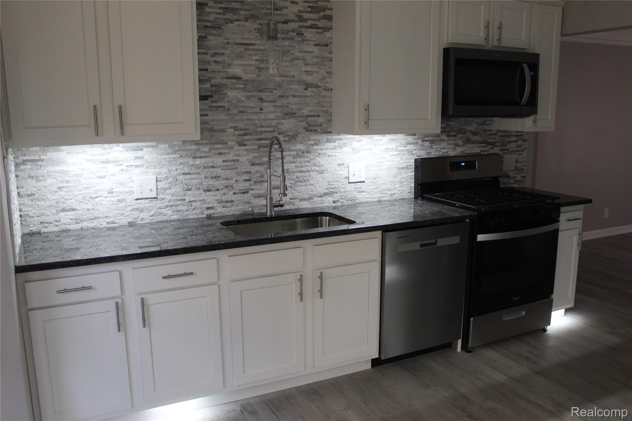 5543 Balfour Road Detroit, MI 48224 - Photo 52 of 54 Modern kitchen featuring white cabinetry with brushed nickel hardware, a multi-tone stacked stone backsplash, dark countertops, and stainless steel appliances