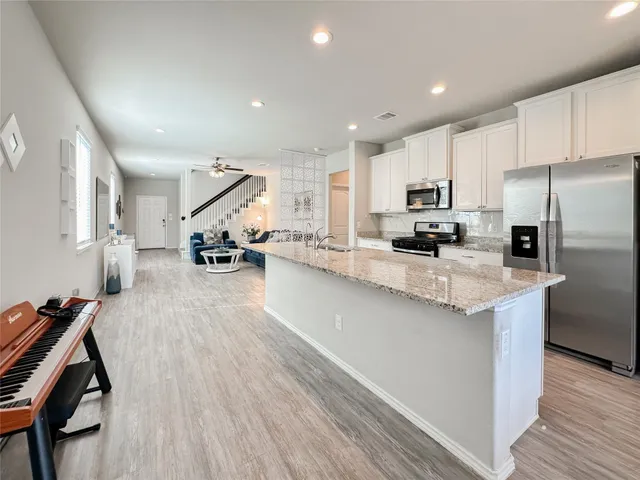 a kitchen with stainless steel appliances kitchen island granite countertop a stove top oven a sink a dining table and chairs with wooden floor