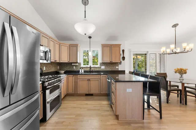 a kitchen with stainless steel appliances granite countertop a refrigerator a stove a sink a dining table and chairs with wooden floor