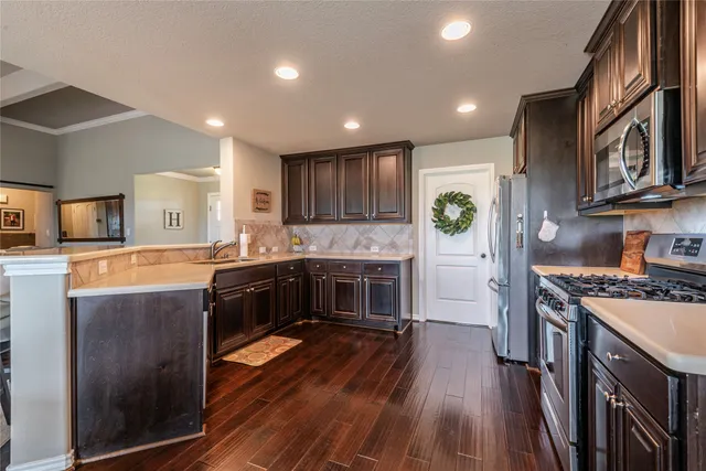 a kitchen with stainless steel appliances granite countertop a stove top oven a sink dishwasher a refrigerator and a cabinets with wooden floor