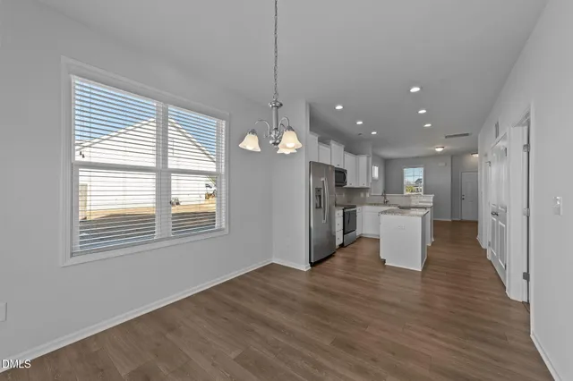 a view of a kitchen and an empty room with wooden floor and windows