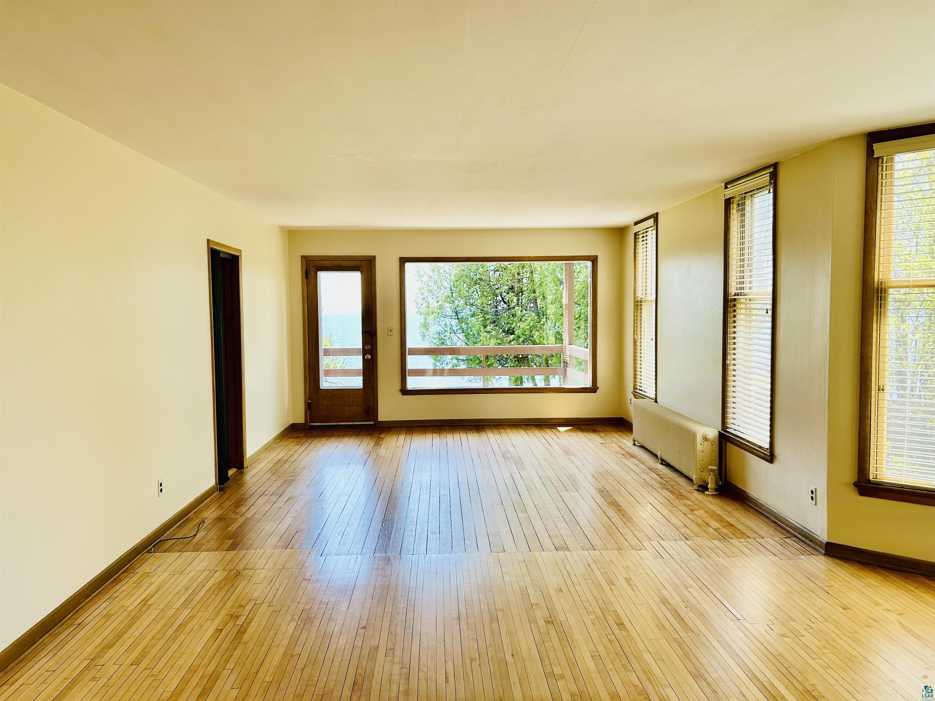 5090 London Road, Unit 1 Duluth, MN 55804 - Photo 16 of 54 Spacious interior room featuring wood-finish flooring, light-colored walls, multiple windows with blinds, a prominent exterior door, and a built-in radiator
