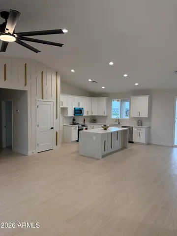 a large white kitchen with stainless steel appliances granite countertop a stove a sink a refrigerator and white cabinets with wooden floor