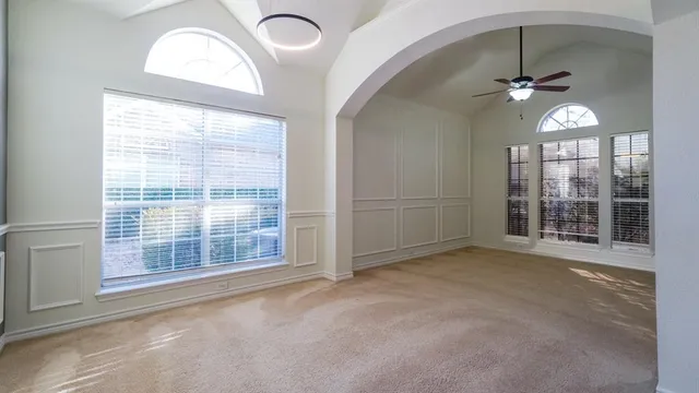 an empty room with chandelier fan and windows