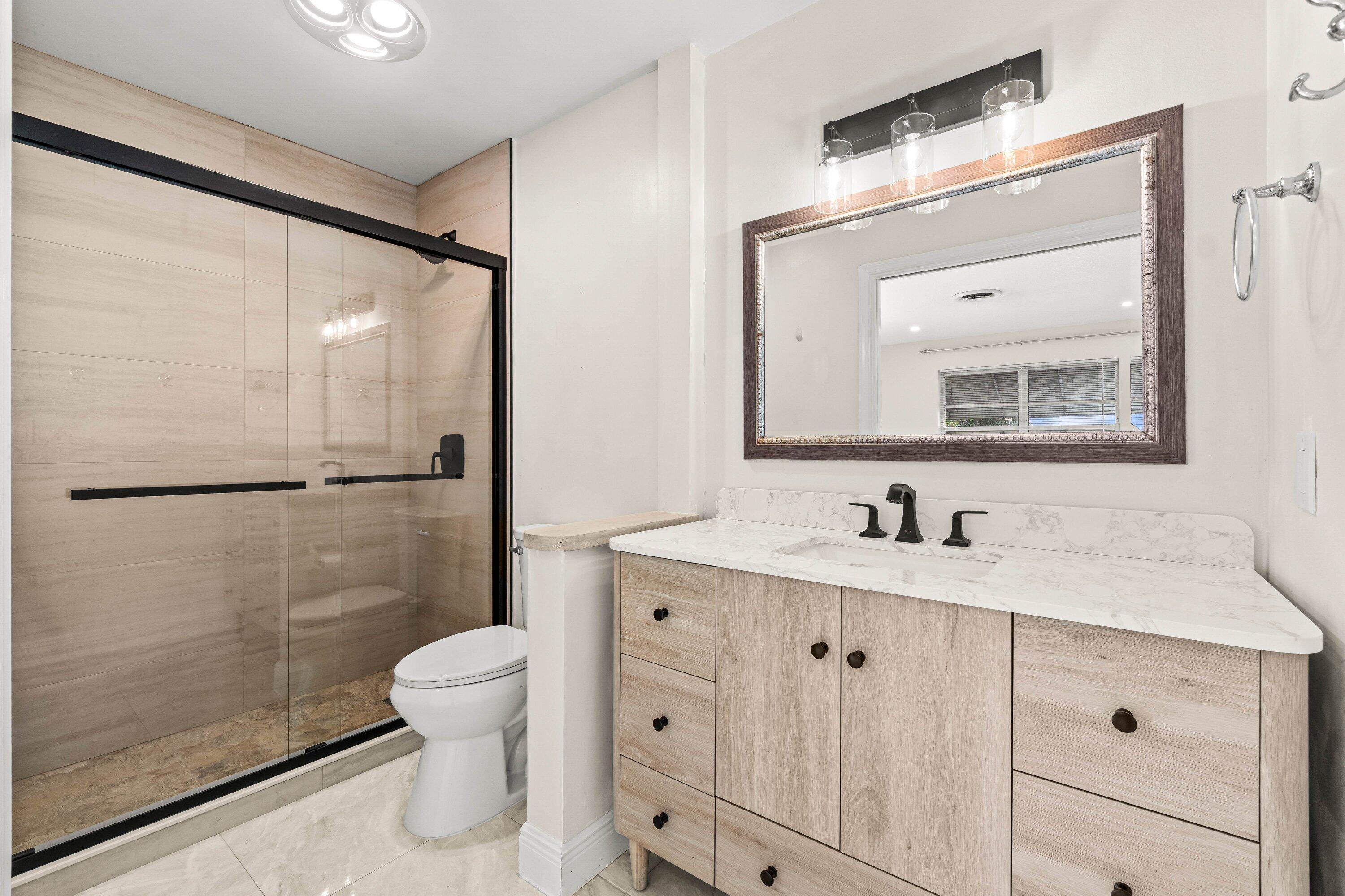 1290 Southwest 8th Street Boca Raton, FL 33486 - Photo 12 of 29 a bathroom with a toilet a sink a glass door a shower a mirror and vanity