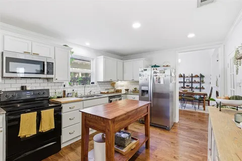 a kitchen with stainless steel appliances a stove a sink a refrigerator white cabinets and wooden floor