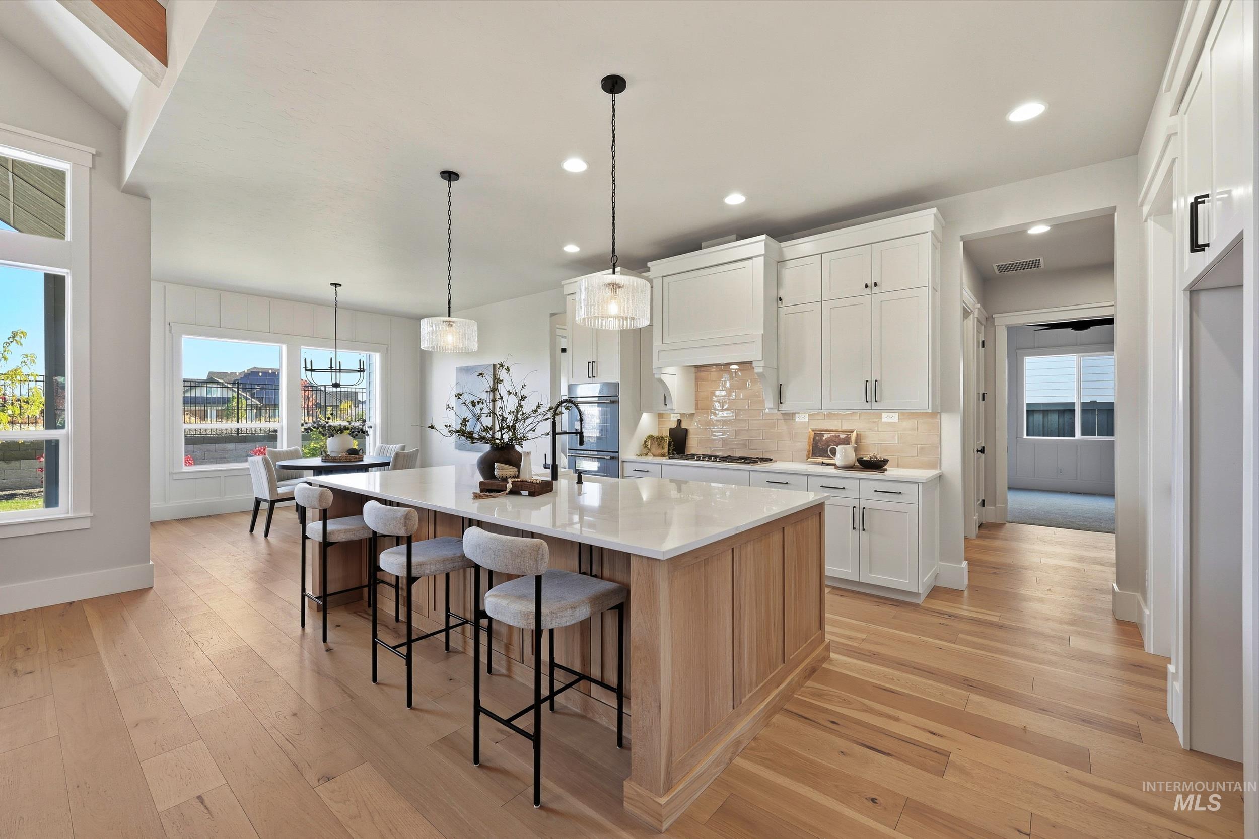 6771 South Messner Way Meridian, ID 83642 - Photo 16 of 45 Kitchen with decorative backsplash, white cabinetry, a breakfast bar area, pendant lighting, and light wood-type flooring